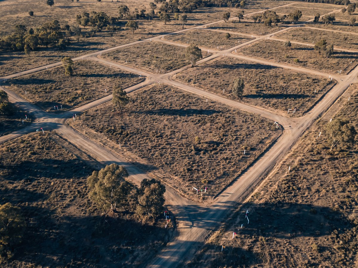 Illustrative aerial photograph of vacant subdivided rural land parcels marked with surveyor stakes, representing the land-banking schemes with no completed development.